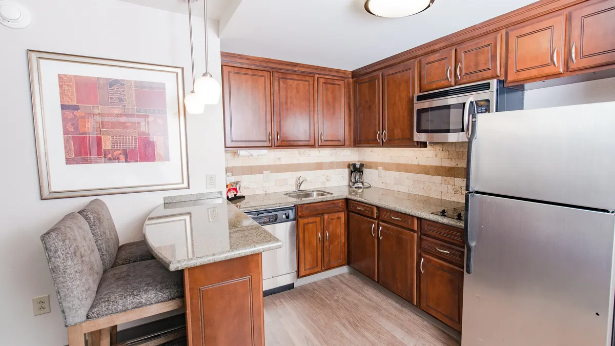 This image features a welcoming kitchen area with granite countertops, wooden cabinetry, stainless steel appliances, and a bar seating area. Framed artwork adds a touch of boutique elegance. The setup is perfect for cooking, entertaining, or casual meals, reinforcing the suite’s functional and inviting atmosphere.