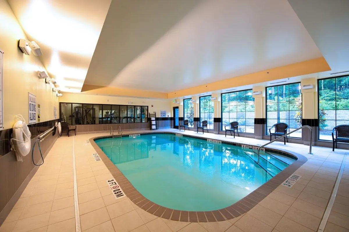 This image offers a view of the indoor pool from a different angle, showing poolside seating and large windows that provide scenic views. The inviting mood and tranquil setting highlight both relaxation and the appeal of spending time by the pool, either swimming or socializing.