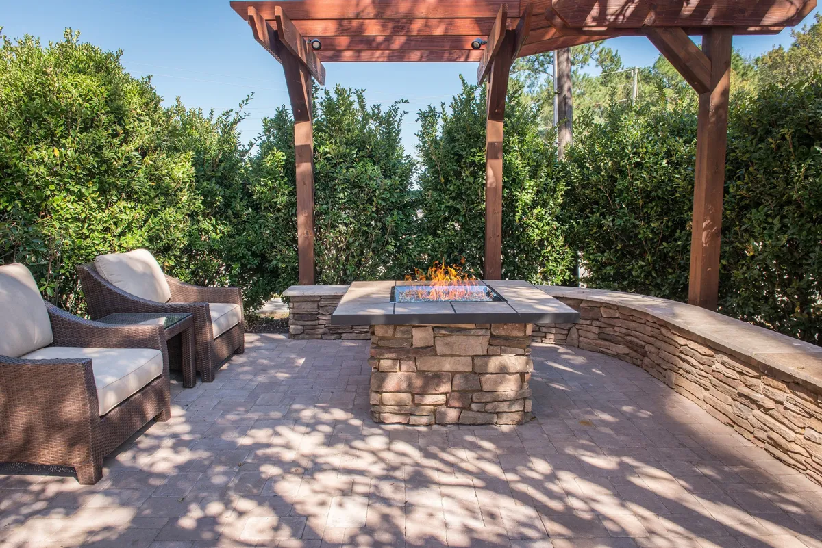 An outdoor setting showing a cozy fire pit area with ample seating under a stylish pergola. The space is designed for relaxation and social gatherings, making it ideal for families to unwind after an adventurous day or to create lasting memories together.