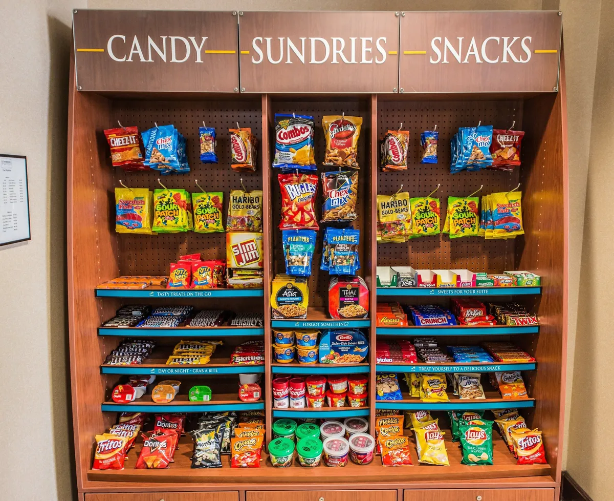 A cheerful interior scene showcasing a sundries shelf stocked with a wide range of candy items, snack packs, and essential travel sundries. The neatly arranged shelves invite guests to quickly grab treats or essentials as needed.