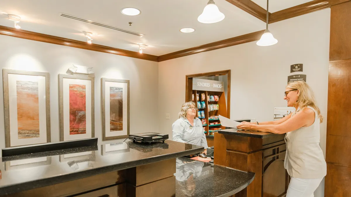 A welcoming hotel interior with a reception desk staffed for guest assistance, tasteful artwork on the wall, and a snack display area. The setting feels friendly and professional, highlighting guest services and convenience.