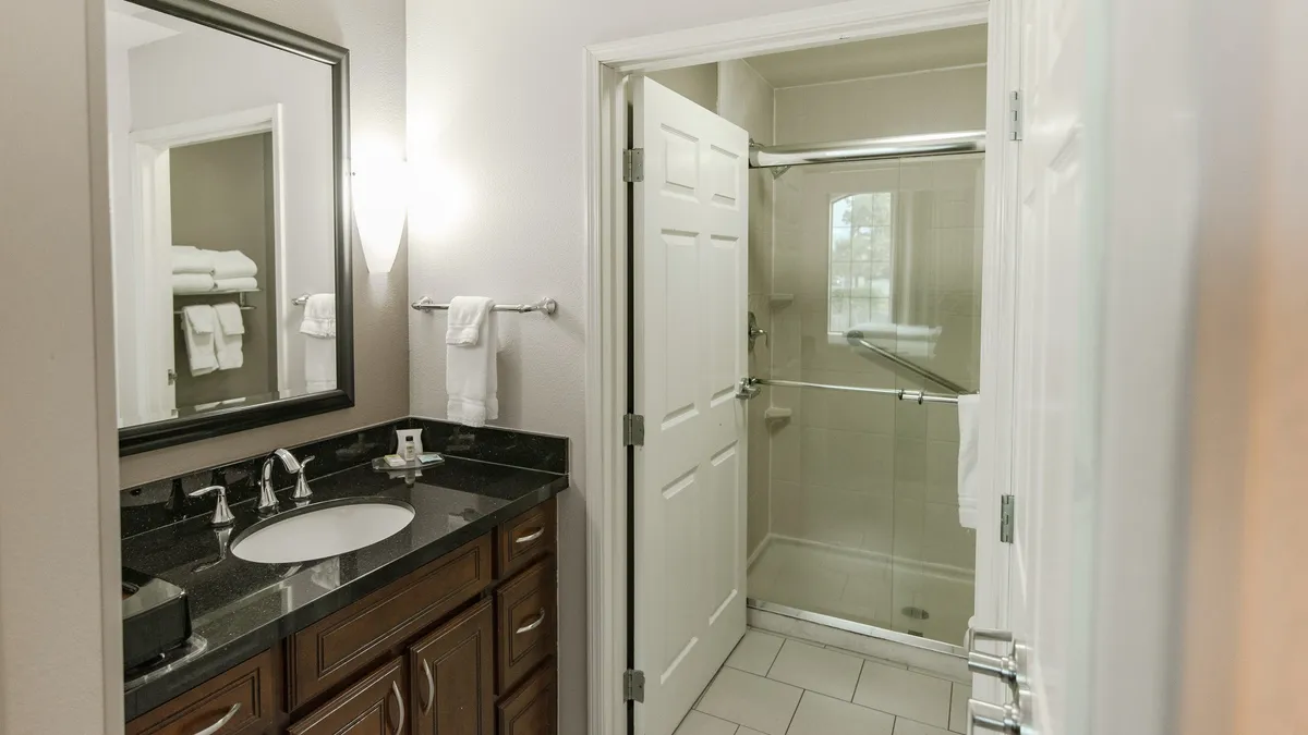 This image features a well-lit bathroom vanity area with a large mirror, a spacious countertop, and a glimpse of the adjoining shower space. The clean lines, ample lighting, and modern fixtures create an inviting and comfortable atmosphere, ideal for daily grooming and relaxation routines.