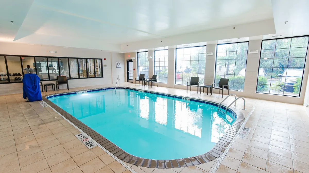 This image features an inviting indoor swimming pool area bathed in natural light from large windows, with comfortable seating arranged around the pool. The ambience is tranquil and provides a space for both relaxation and social interaction.